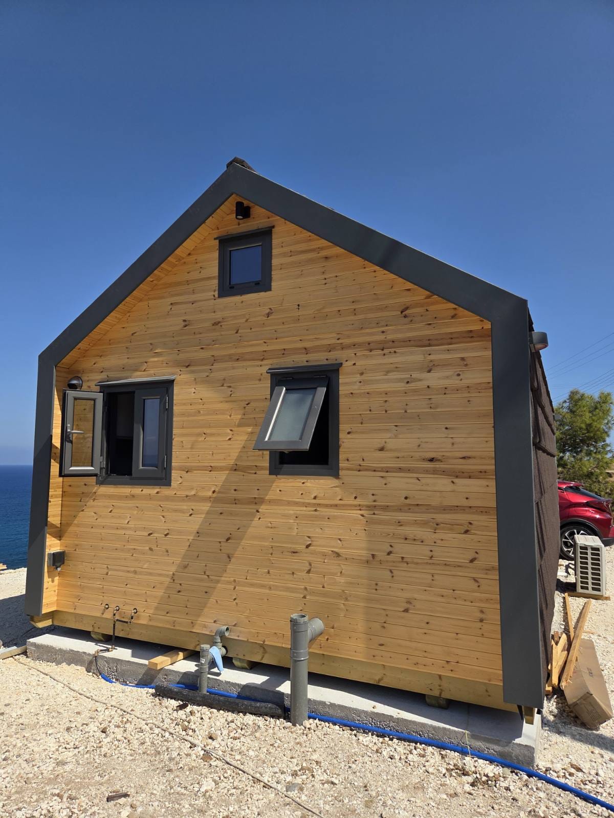 Wooden cabin with a red vehicle in the background. Prefab house Cyprus. Prefabricated modular home Cyprus. Prefabcy. Buy modular home in Cyprus.