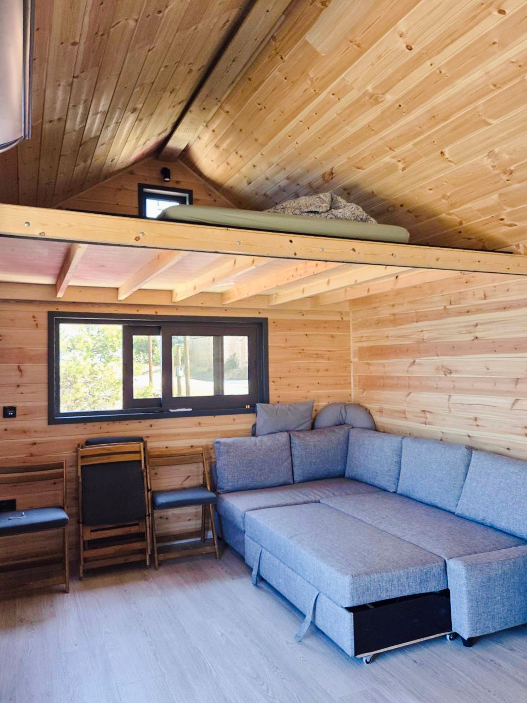 Cozy living room with wooden walls and ceiling, featuring a blue sofa and a small table. Prefab house Cyprus. Prefabricated modular home Cyprus. Prefabcy. Buy modular home in Cyprus.