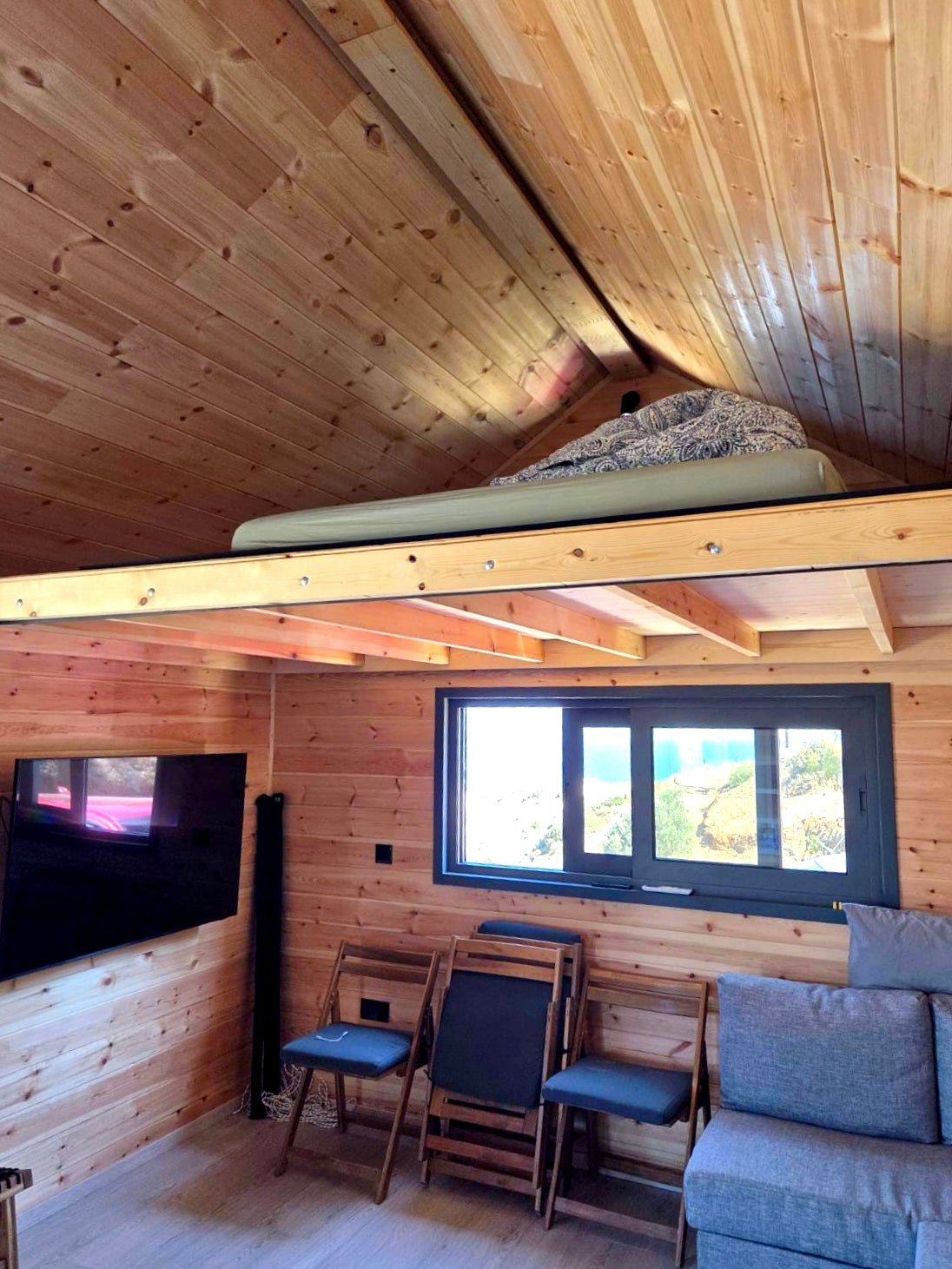 Wooden interior with a loft bed, TV, and seating area. Prefab house Cyprus. Prefabricated modular home Cyprus. Prefabcy. Buy modular home in Cyprus.