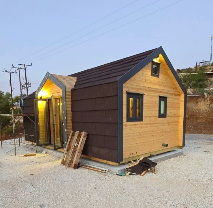 Small wooden cabin with brown roof and black trim on a gravel surface. Prefab house Cyprus. Prefabricated modular home Cyprus. Prefabcy. Buy modular home in Cyprus.