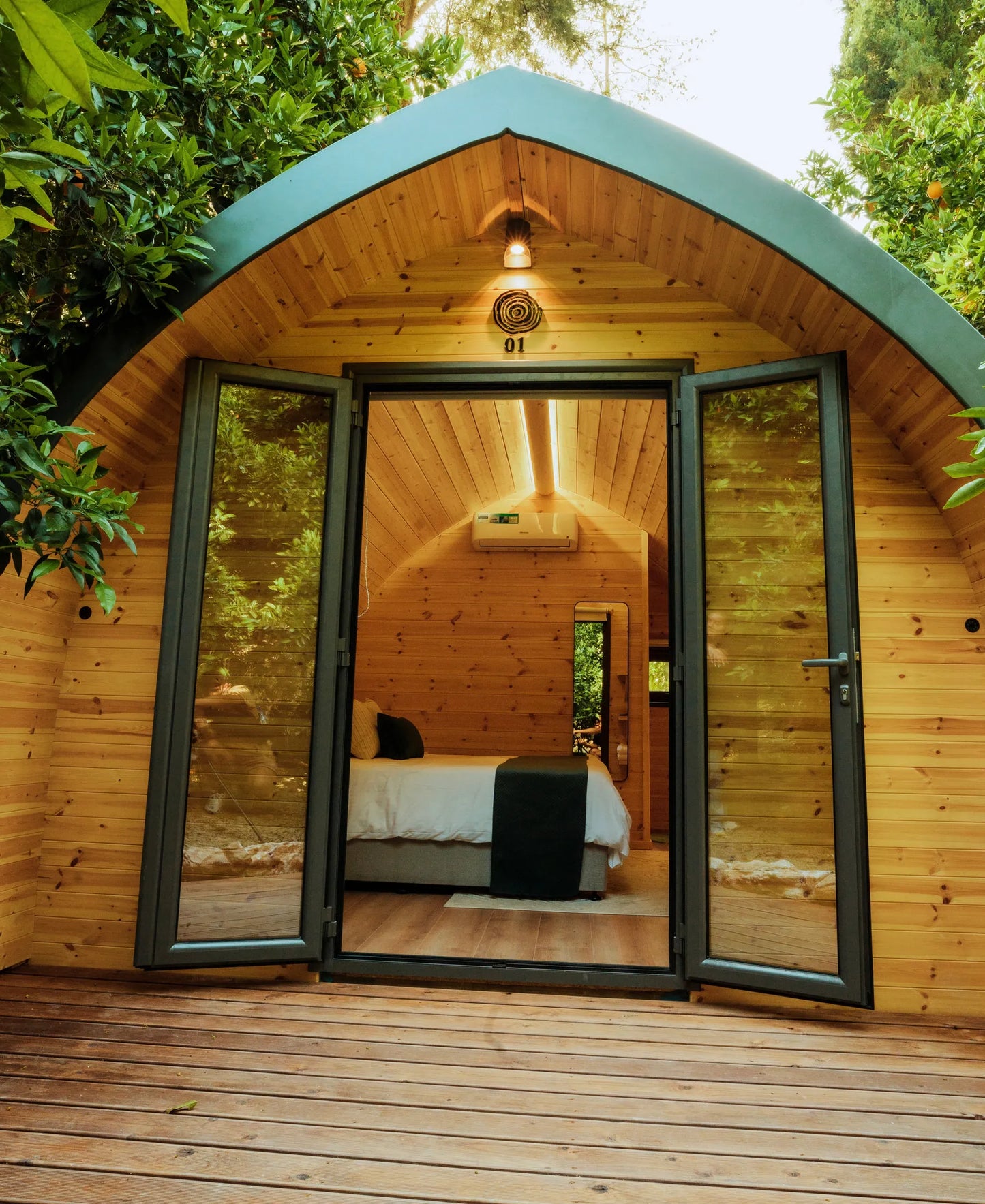 Wooden cabin with open doors revealing a bedroom interior, surrounded by greenery. Prefabcy.com, prefab home Cyprus, prefabricated modular house, buy in Cyprus