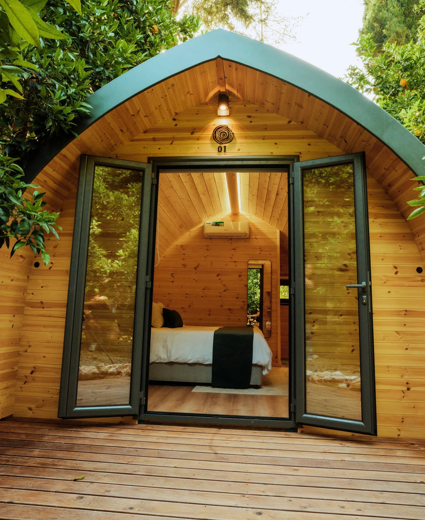 Wooden cabin with open doors revealing a bedroom interior, surrounded by greenery. Prefabcy.com, prefab home Cyprus, prefabricated modular house, buy in Cyprus
