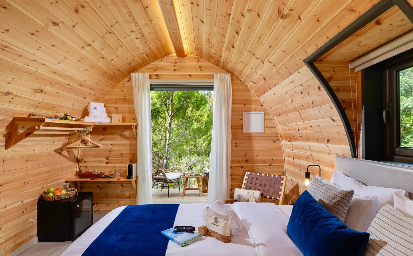 Wooden cabin interior with a bed, shelves, and a view of greenery outside. Prefab house Cyprus. Prefabricated modular home Cyprus. Prefabcy. Buy modular home in Cyprus.